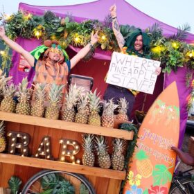 Two people standing behind a bar holding a 'Where's Pineapple Steve' sign.